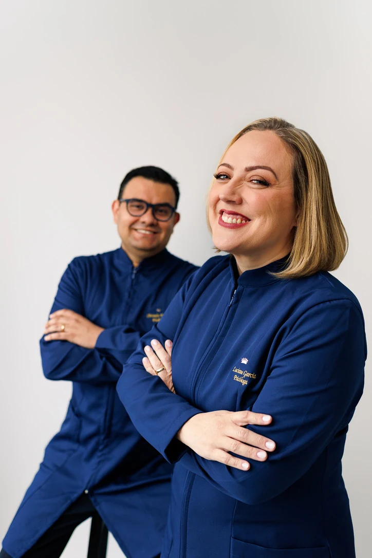 Luciane e Christofer, psicólogos da Garcia Valenço Psicologia, sorrindo e vestindo jalecos azul-marinho
